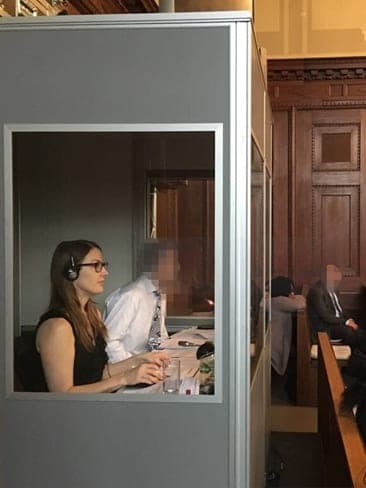 Viviane Murray McCain interpreting from a booth, wearing a headset, during a hearing in a wood-panelled courtroom.